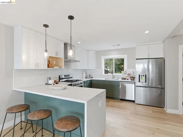 Kitchen featuring a peninsula, a breakfast bar, stainless steel appliances, decorative light fixtures, and light stone counters