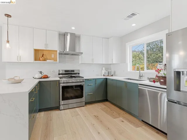 Kitchen featuring dual tone cabinetry, stainless steel appliances, light stone counters, and light wood-style floors