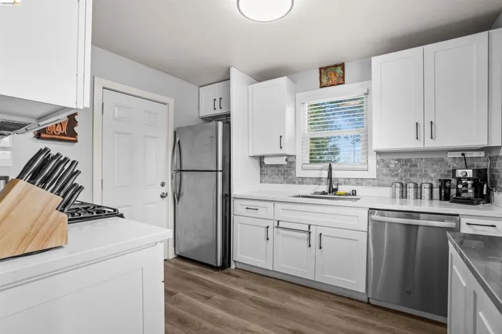 Kitchen with stainless steel appliances, dark wood-style floors, white cabinets, backsplash, and light stone counters