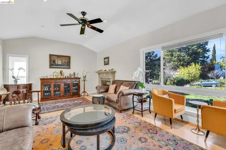 Living room with a ceiling fan, vaulted ceiling, light wood-style floors, and a fireplace