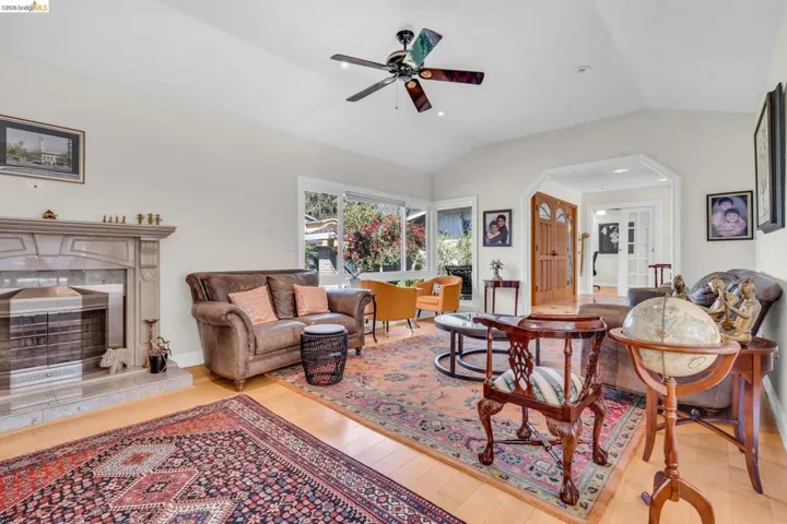 Living room featuring a premium fireplace, light wood finished floors, arched walkways, vaulted ceiling, and a ceiling fan