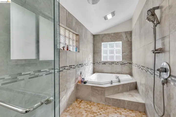 Full bath with vaulted ceiling, tile walls, a stall shower, and a bath