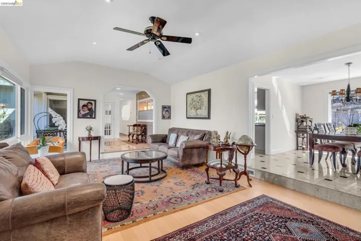 Living room featuring healthy amount of natural light, arched walkways, lofted ceiling, ceiling fan, and light wood-type flooring
