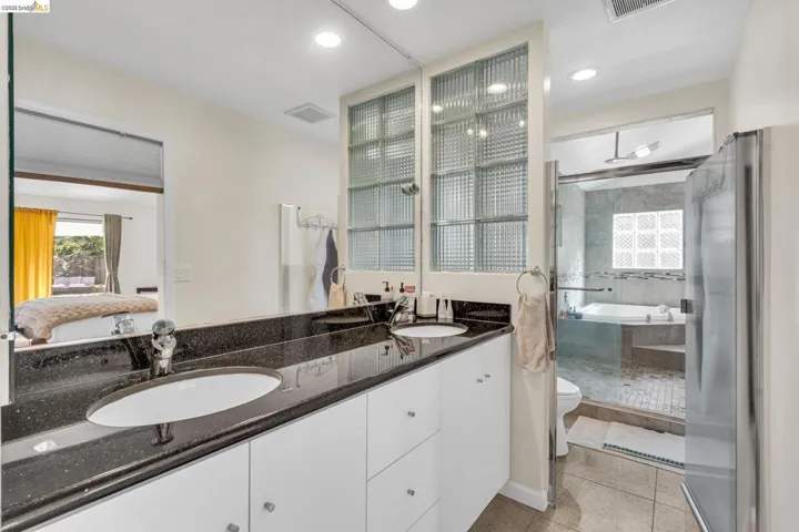 Ensuite bathroom featuring double vanity, light tile patterned floors, a shower stall, and recessed lighting