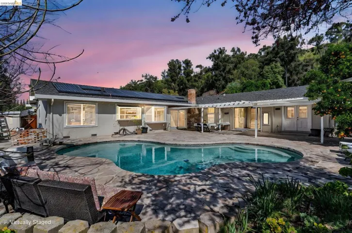 Back of house at dusk featuring a patio, roof mounted solar panels, an outdoor pool, a chimney, and crawl space