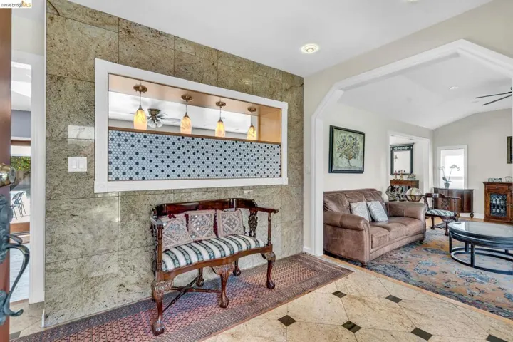 Living area featuring a ceiling fan, tile walls, and inlaid floor details