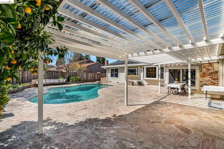 View of swimming pool with patio surround, outdoor dining space, a fenced backyard, and a pergola