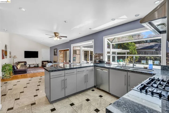 Kitchen with gray cabinets, exhaust hood, dishwasher, a skylight, and a ceiling fan