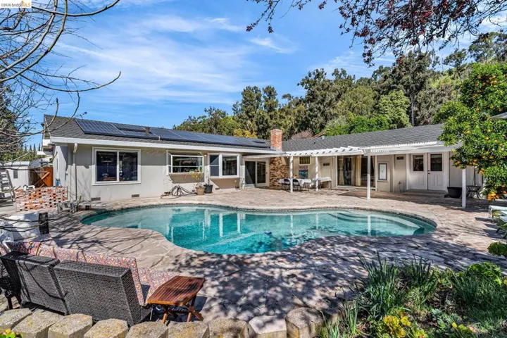 Rear view of property featuring a patio area, solar panels, a chimney, and an outdoor pool
