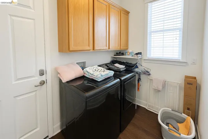 Washroom featuring dark wood-style flooring, washer and clothes dryer, and cabinet space