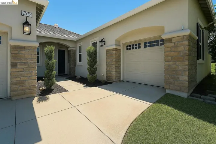 View of property exterior with stone siding, stucco siding, driveway, and a garage