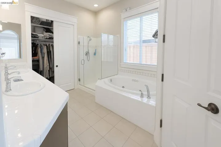 Bathroom with a shower stall, a whirlpool tub, a spacious closet, light tile patterned flooring, and double vanity