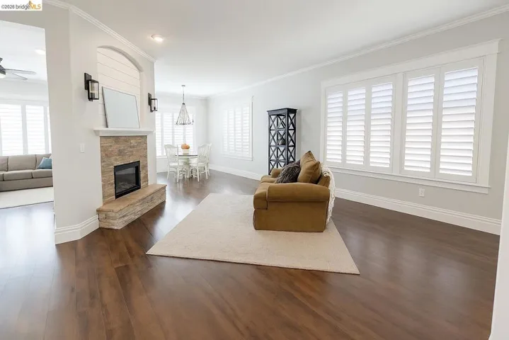 Living room with ornamental molding, dark wood-type flooring, healthy amount of natural light, a fireplace, and ceiling fan