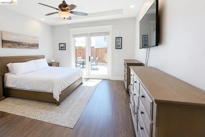 Bedroom with dark wood-style floors, access to exterior, ceiling fan, recessed lighting, and a raised ceiling