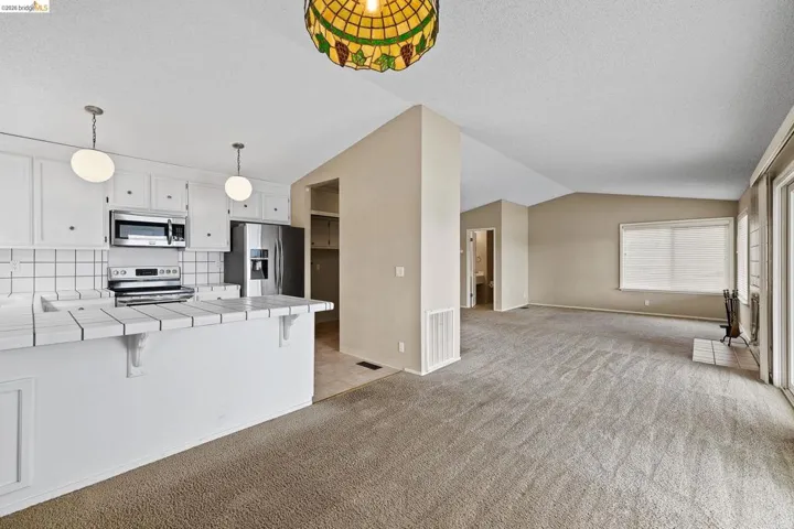 Kitchen featuring a breakfast bar, tile countertops, white cabinets, stainless steel appliances, and tasteful backsplash