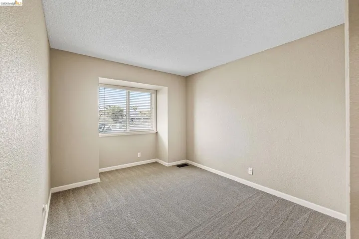 Empty room with a textured wall, light carpet, and a textured ceiling