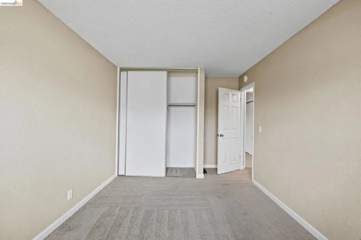 Unfurnished bedroom featuring a textured wall, light carpet, a closet, and a textured ceiling