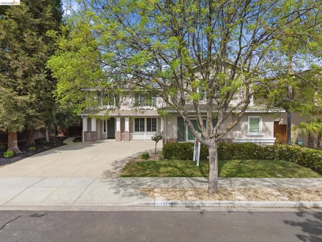 View of property hidden behind natural elements featuring concrete driveway, covered porch, and brick siding