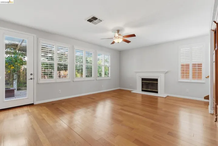 Unfurnished living room with light wood-style flooring, ceiling fan, plenty of natural light, and a glass covered fireplace