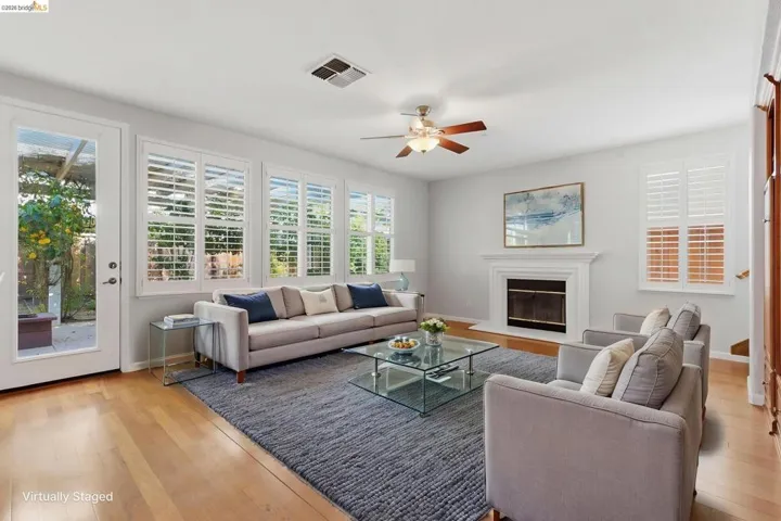 Living room featuring light wood finished floors, ceiling fan, a glass covered fireplace, and healthy amount of natural light
