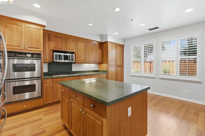 Kitchen with stainless steel appliances, wood finish cabinetry, light wood-style floors, a kitchen island, and recessed lighting