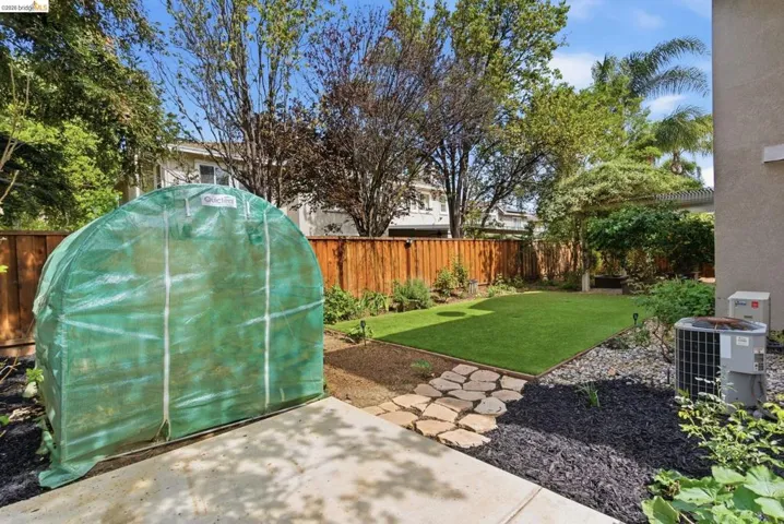 Fenced backyard featuring a greenhouse, an outbuilding, and a patio