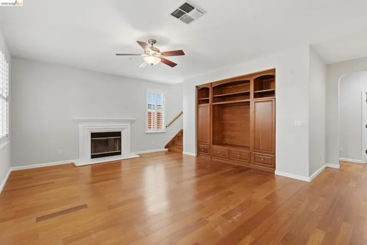 Unfurnished living room with arched walkways, light wood-style floors, a glass covered fireplace, and ceiling fan