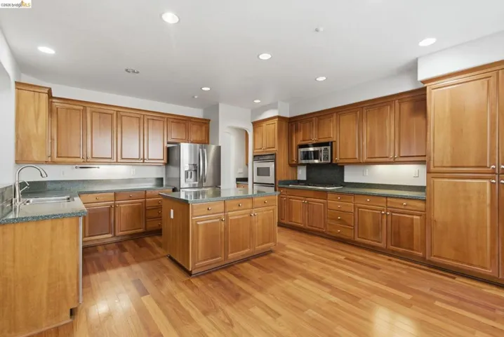 Kitchen featuring stainless steel appliances, light wood-style floors, wood finish cabinetry, a center island, and arched walkways