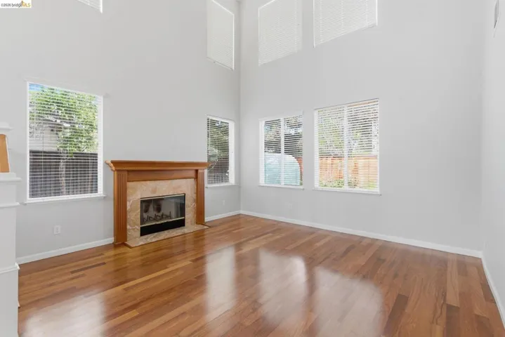 Unfurnished living room with wood finished floors, a tiled fireplace, and a high ceiling