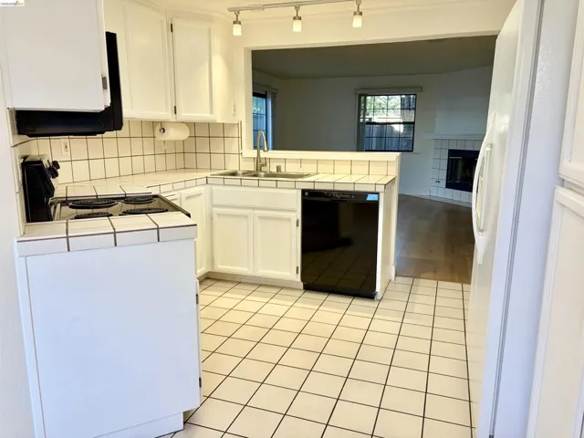 Kitchen featuring tile counters, white cabinets, black dishwasher, and decorative backsplash