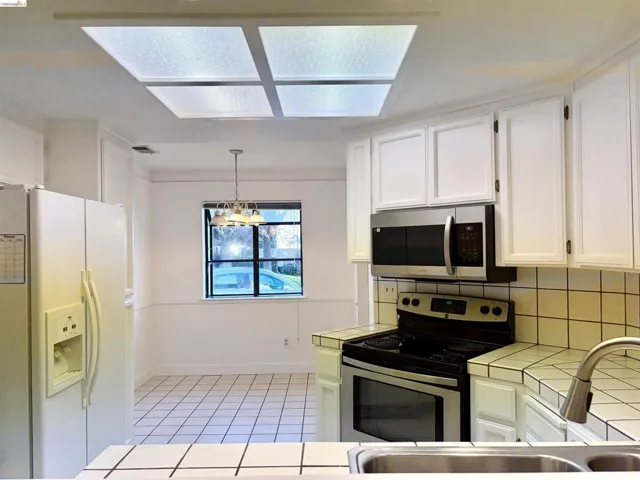Kitchen featuring stainless steel appliances, white cabinetry, tile countertops, backsplash, and light tile patterned floors