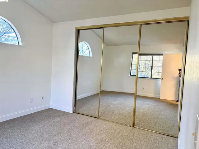 Unfurnished bedroom with multiple windows, a closet, vaulted ceiling, light colored carpet, and a textured ceiling