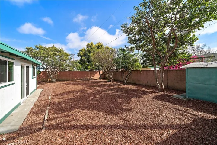 The large wrap-around backyard is a private blank canvas ready for your imagination, featuring block wall fencing, multiple fruit trees including avocado, and two large storage sheds, offering endless possibilities for entertaining, gardening, or a future ADU.