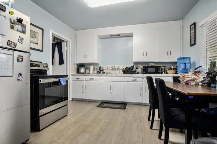 Kitchen with tile counters, freestanding refrigerator, electric range, white cabinetry, and black microwave