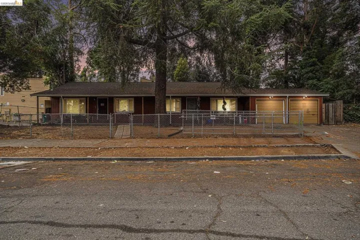 Single story home featuring an attached garage, a fenced front yard, a gate, driveway, and a shingled roof