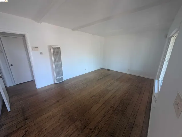 Unfurnished room with beamed ceiling, a heating unit, and dark wood finished floors