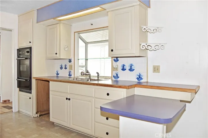 Happy kitchen with wall oven, dual stainless sinks, garden window, refrigerator (new in 2024), gas cooktop, small breakfast bar, lazy Susan pantry, blue accents, and whimsical windmills
