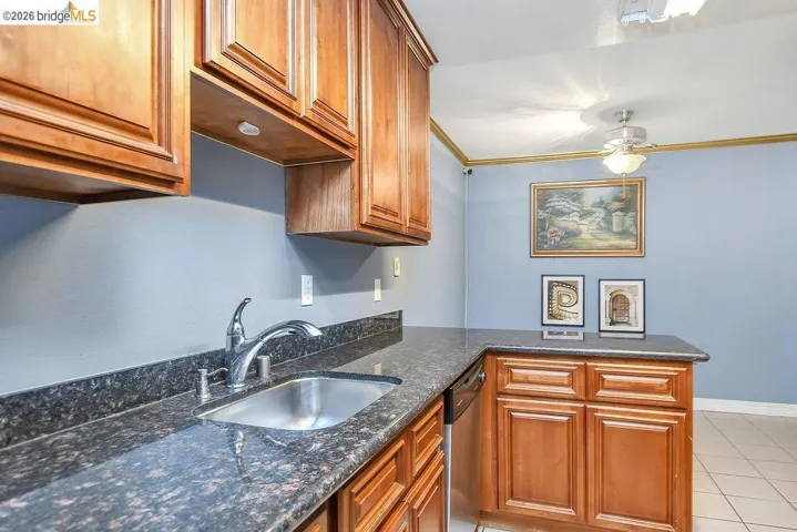 Kitchen featuring a peninsula, brown cabinetry, dark stone counters, dishwasher, and light tile patterned floors
