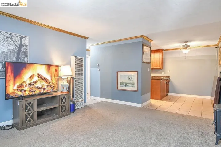 Living room featuring light carpet, a heating unit, ornamental molding, a ceiling fan, and light tile patterned flooring