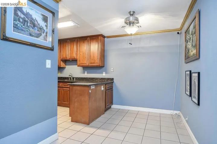 Kitchen with brown cabinetry, dark stone counters, light tile patterned floors, crown molding, and a peninsula