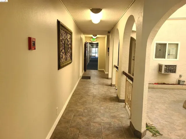 Corridor featuring stone finish floors, a textured wall, arched walkways, and a textured ceiling