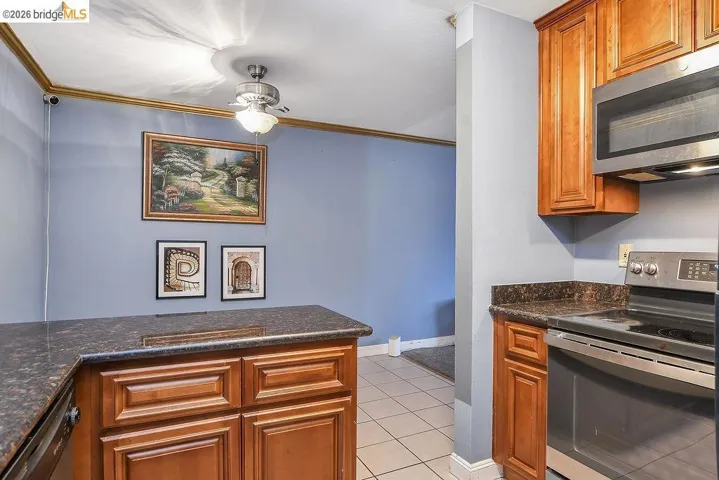 Kitchen with appliances with stainless steel finishes, brown cabinetry, dark stone counters, and crown molding