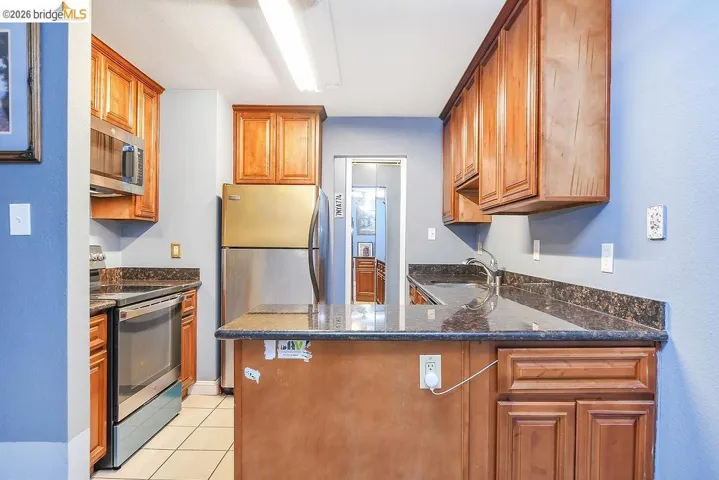 Kitchen featuring stainless steel appliances, dark stone countertops, brown cabinets, and a peninsula
