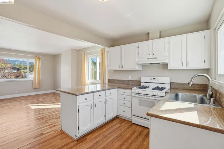 Kitchen featuring white gas range, white cabinets, light wood-style flooring, a peninsula, and light stone counters