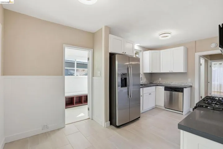 Kitchen featuring stainless steel appliances, white cabinetry, wainscoting, and dark stone counters