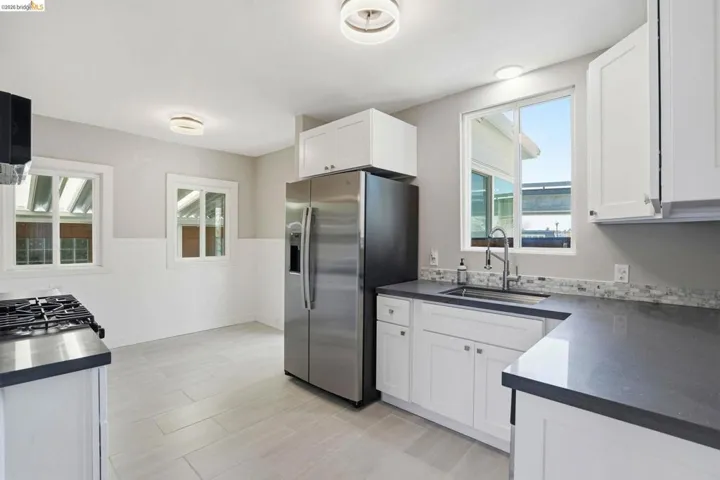 Kitchen featuring wainscoting, stainless steel refrigerator with ice dispenser, white cabinets, and dark stone counters