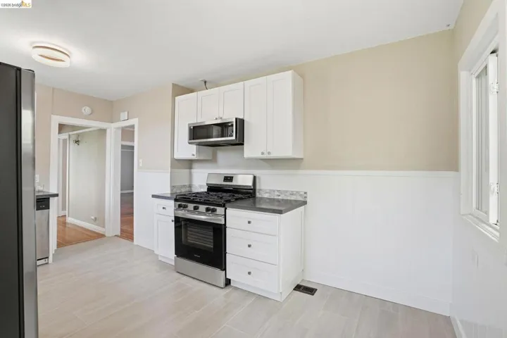 Kitchen featuring stainless steel appliances, white cabinets, a wainscoted wall, and dark countertops