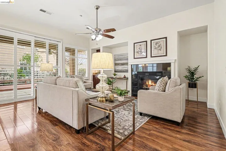 Living area featuring dark wood-style flooring, ceiling fan, and a tiled fireplace