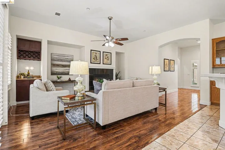 Living room featuring a tiled fireplace, wood-type flooring, arched walkways, ceiling fan, and plenty of natural light