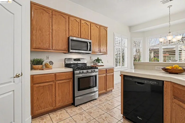 Kitchen featuring stainless steel appliances, tile counters, wood finish cabinetry, a chandelier, and light tile patterned floors